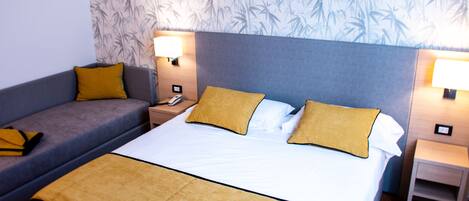 A hotel room with a bed, a sofa, two nightstands, and a wall with a bamboo pattern.