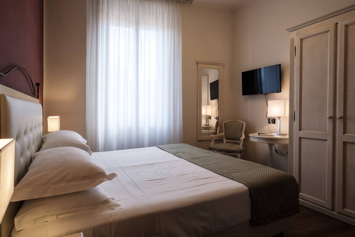 A hotel room with a large bed, a television, a desk with a lamp, and a wardrobe.