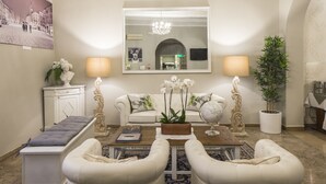Una sala de estar con un sofá, dos sillones, una mesa de centro y una mesita auxiliar con una lámpara. Hay un espejo sobre el sofá y una planta en la mesita.