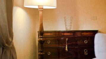 A wooden dresser with a glass vase, a lamp, and a light switch on the wall.