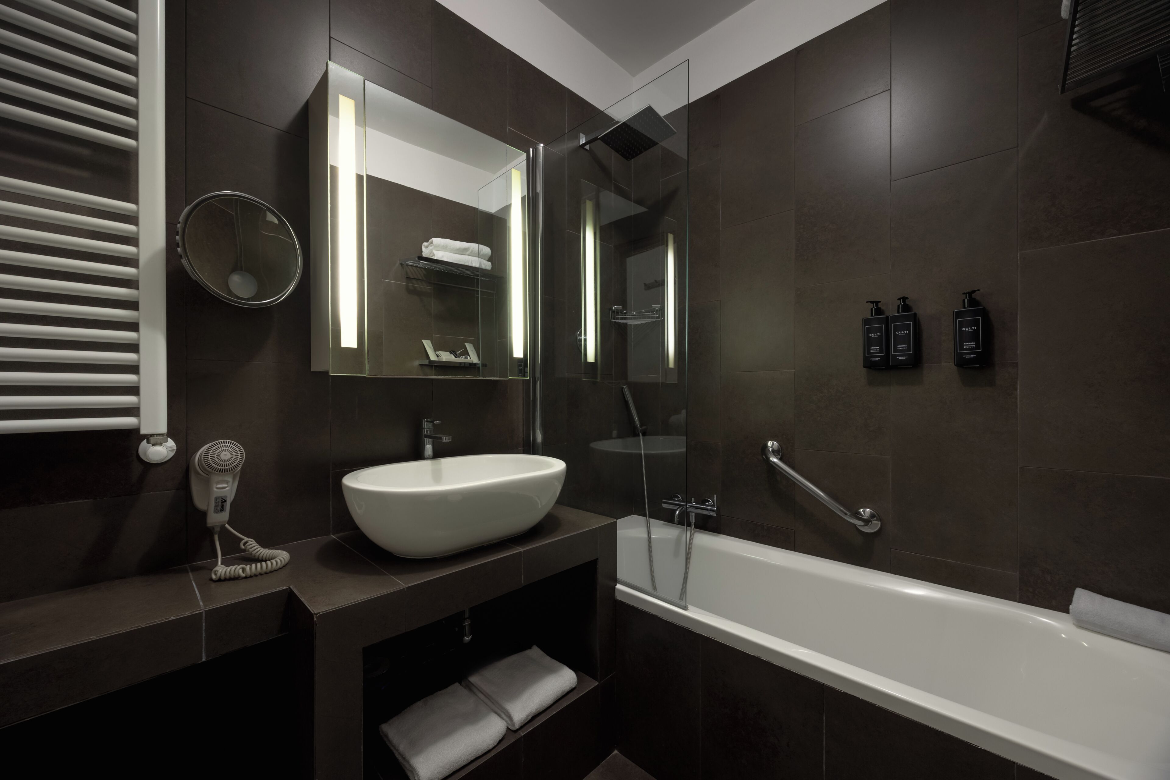 Un bagno moderno con un lavandino bianco capiente, una cabina doccia in vetro e pareti rivestite di piastrelle scure.
