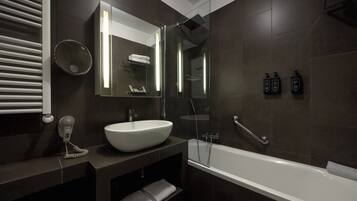 Un bagno moderno con un lavandino bianco capiente, una cabina doccia in vetro e pareti rivestite di piastrelle scure.