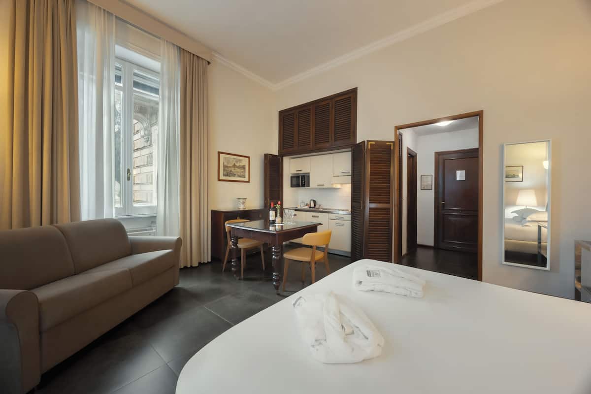 Une chambre d’hôtel comprenant un canapé, une table à manger avec des chaises, un coin cuisine et un lit avec des serviettes.