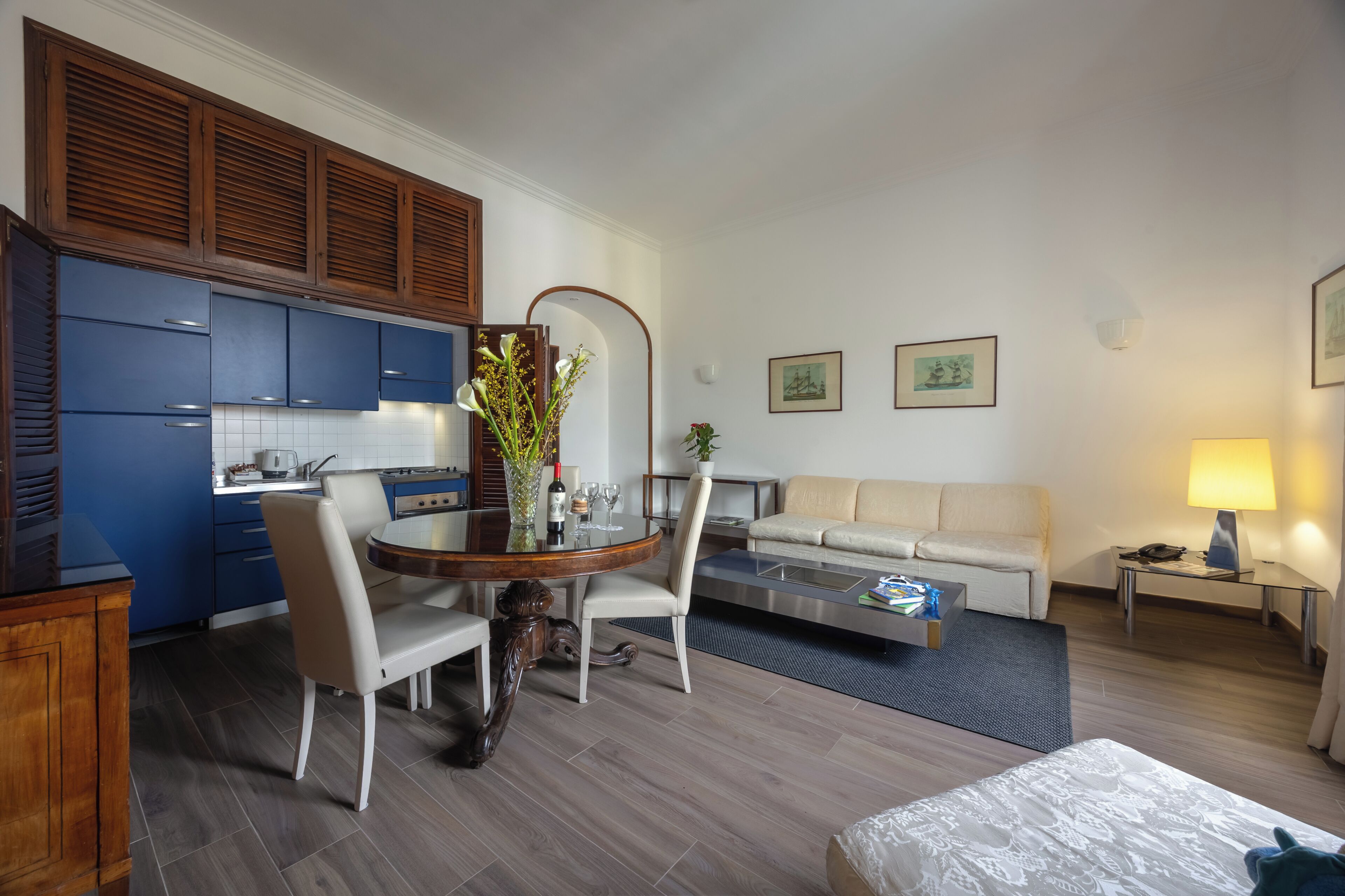 Een moderne hotelkamer met een zithoek, kitchenette, sofa en een klein tafeltje met een lamp.