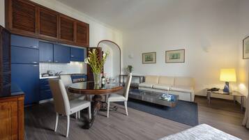 Een moderne hotelkamer met een zithoek, kitchenette, sofa en een klein tafeltje met een lamp.