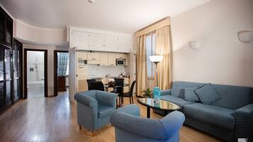 Un salon moderne avec un canapé bleu, deux fauteuils, une table basse et une cuisine en arrière-plan.