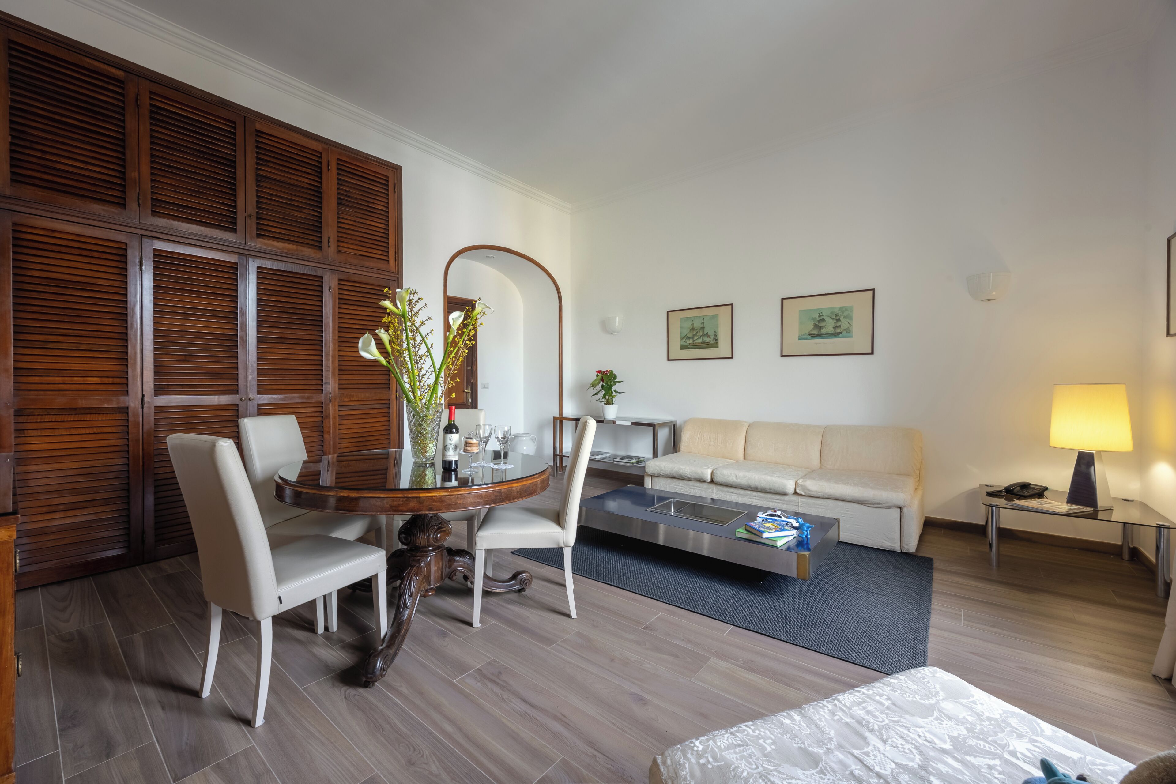 A modern hotel room with a dining table, chairs, a sofa, a coffee table, and a lamp.