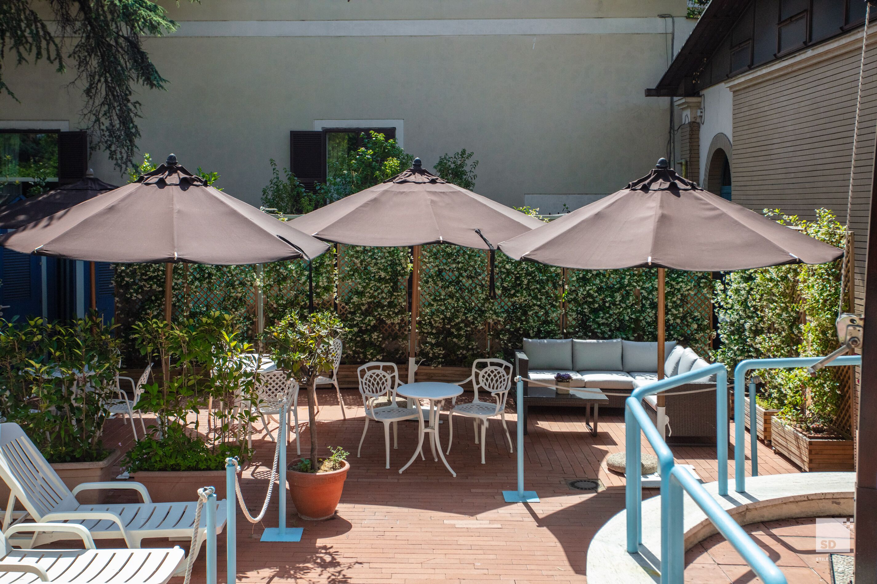 Un espace extérieur aménagé en terrasse, avec trois parasols, des fauteuils de jardin blancs et un canapé blanc.