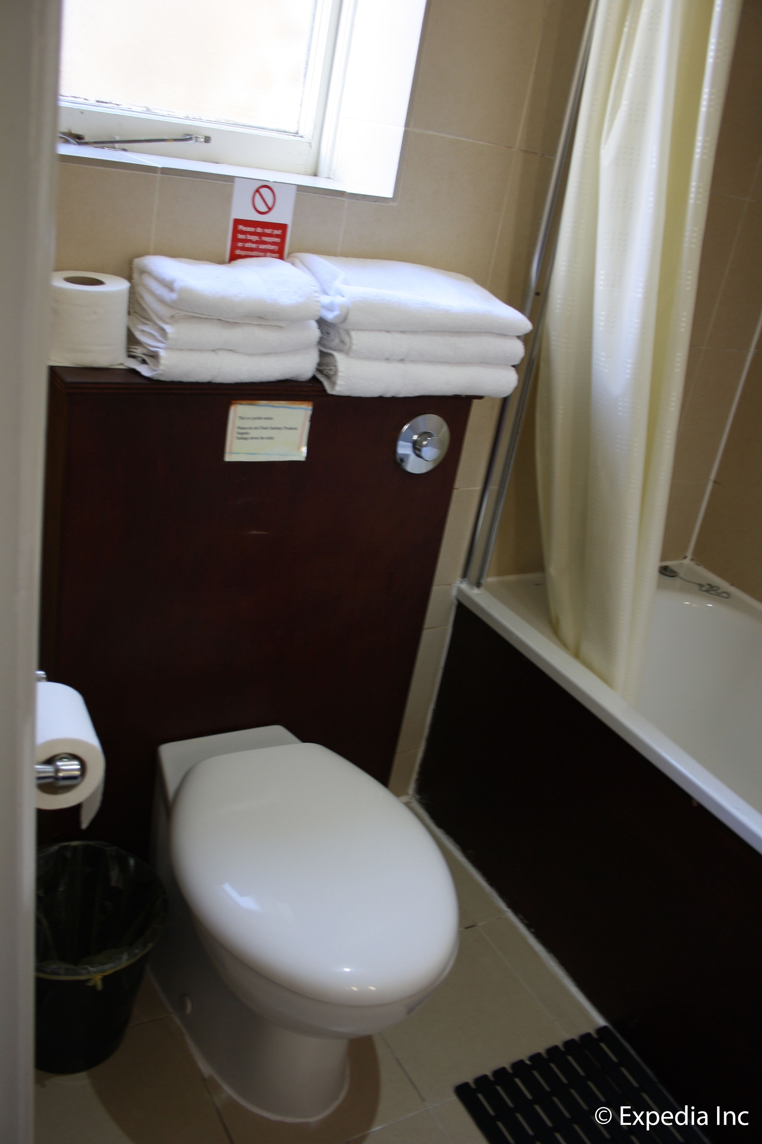 Une petite salle de bain avec des toilettes, une pile de serviettes blanches, un rouleau de papier toilette et un rideau de douche.