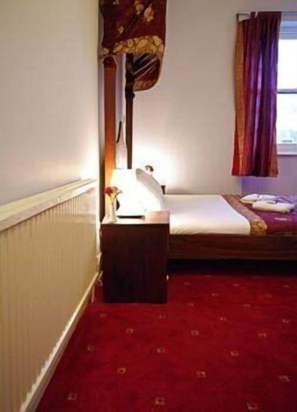 Une petite chambre avec un lit simple, une tête de lit en bois, une table de chevet et une fenêtre avec des rideaux.
