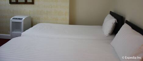 A hotel room with a bed, a wall-mounted mirror, a decorative wall piece, and an air conditioning unit.