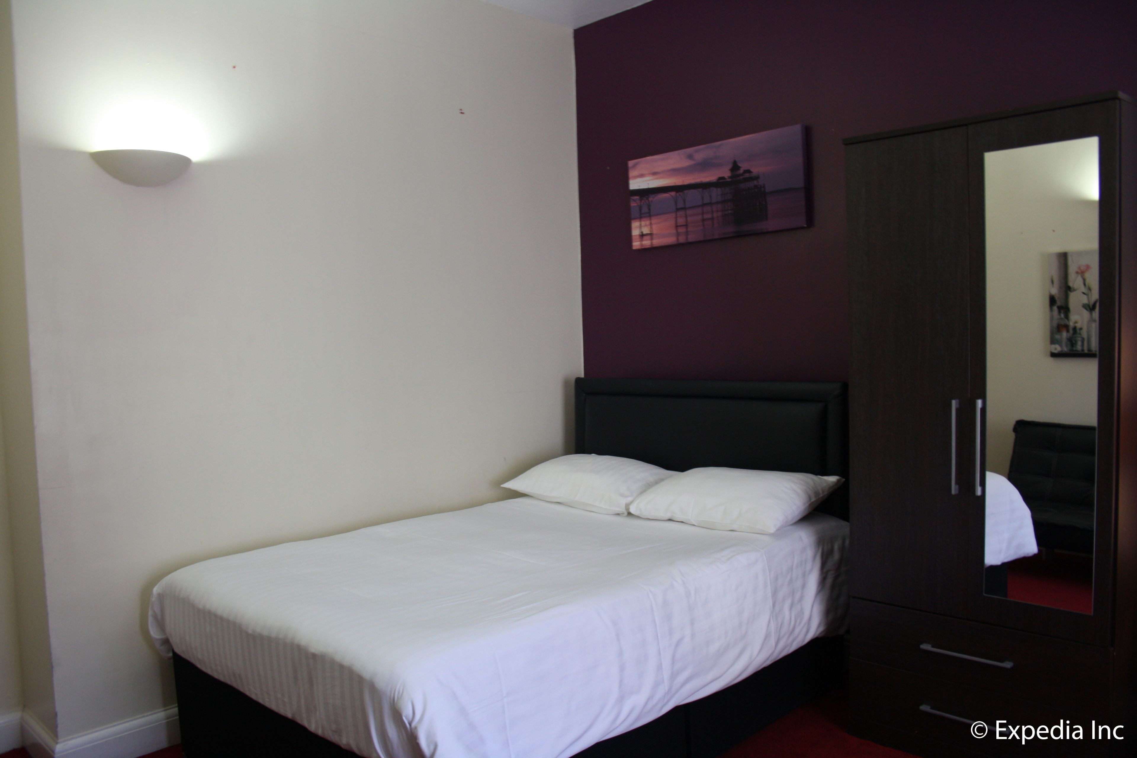 A bedroom with a single bed, a dark wardrobe, a wall-mounted light, and a framed picture.