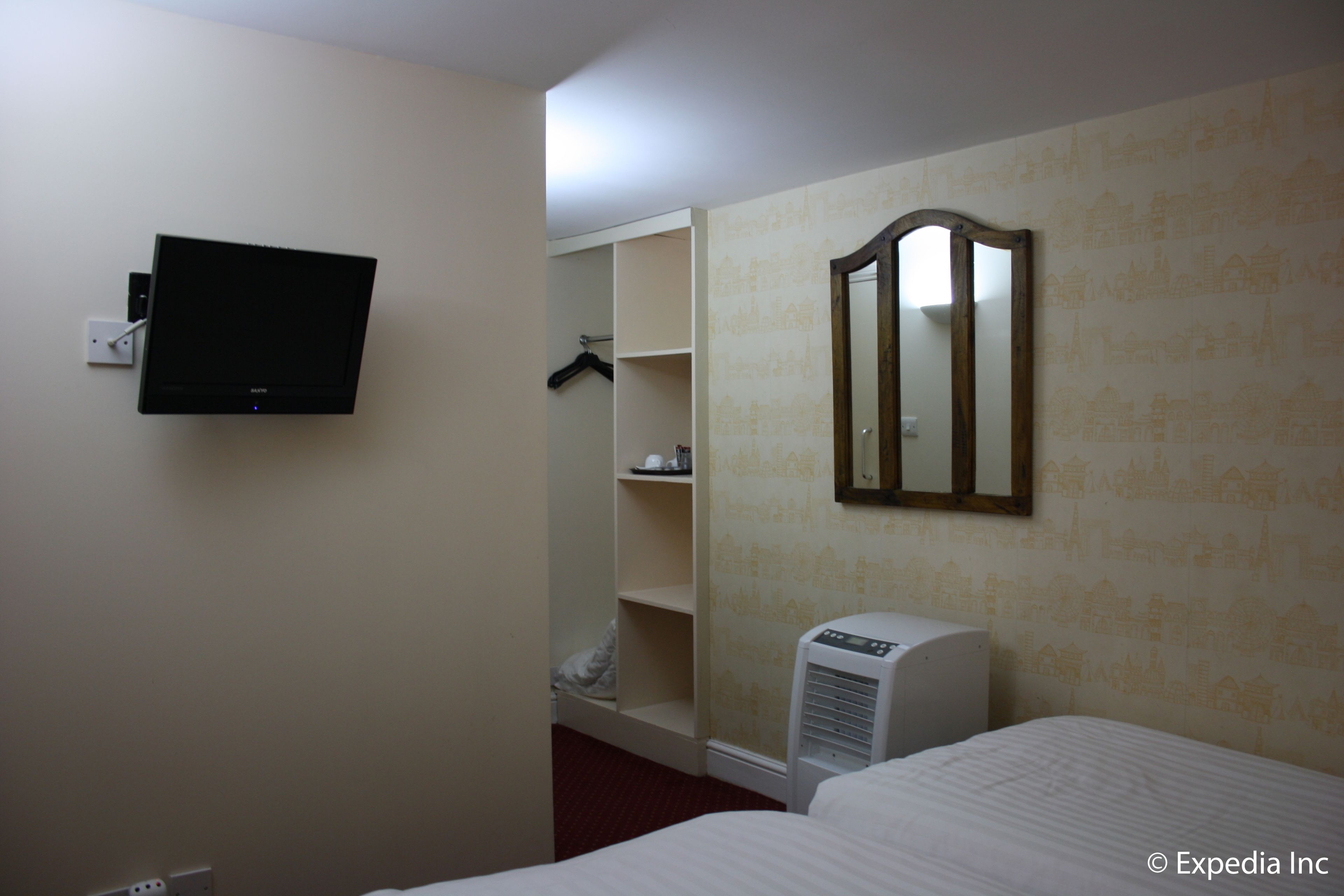 A hotel room with a bed, a TV mounted on the wall, a mirror, and a wardrobe.
