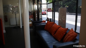 A lobby with a black leather sofa, orange cushions, a map display, and a sign for 24-hour mini cab service. - Islington Inn (London)