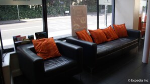 A modern hotel lobby with leather sofas and orange cushions, large windows offering a view of the street, and a reception desk with informational materials. - Islington Inn (London)