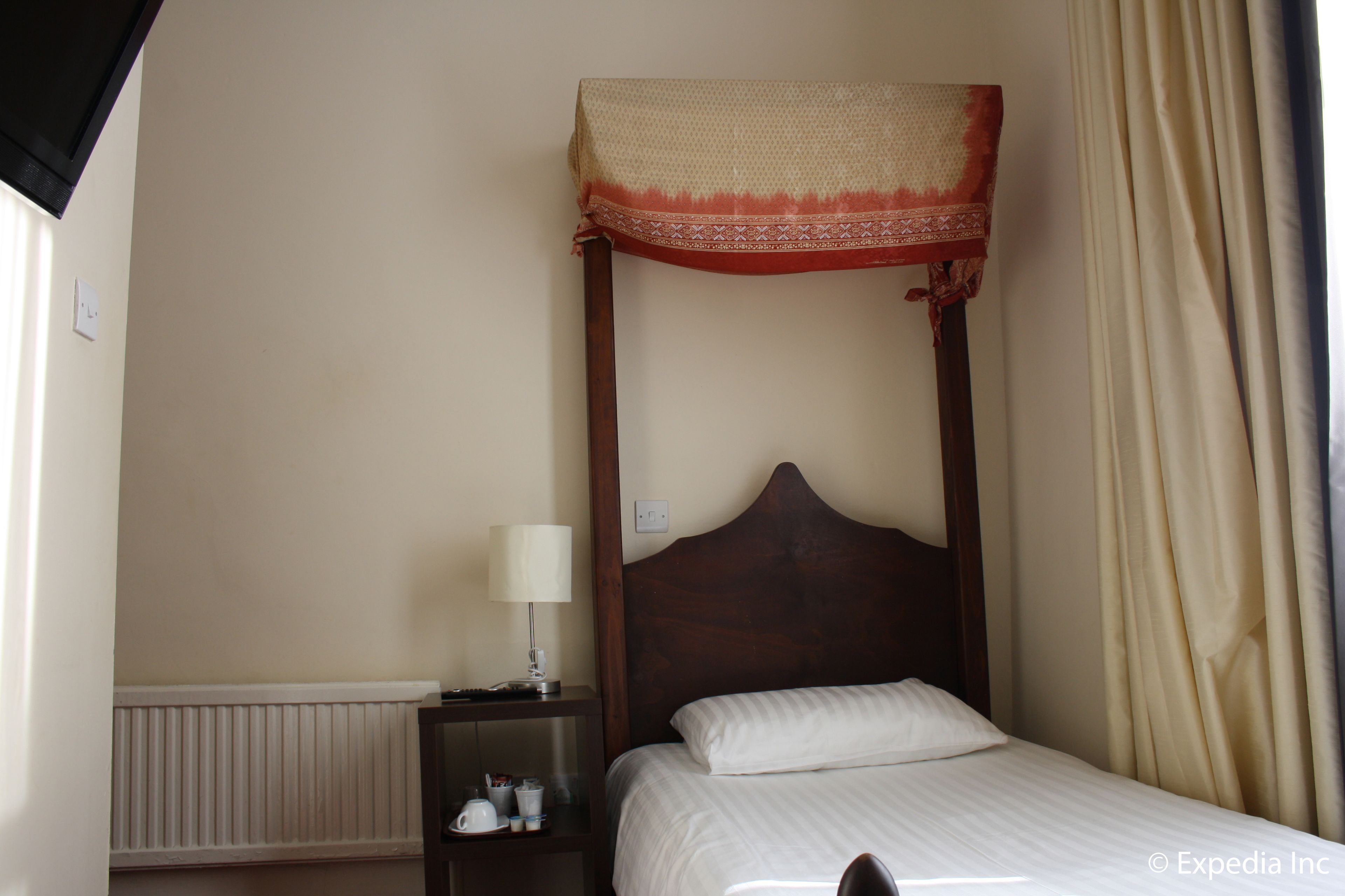 A four-poster bed with a canopy, a bedside table with a lamp, and a nightstand with a cup and saucer.