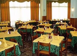 A banquet hall with multiple tables set for dining, each with a green tablecloth and yellow napkins. - Hotel American (Jesolo)