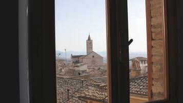 Vista a través de una ventana que muestra un edificio con una torre de campanas y una iglesia al fondo.