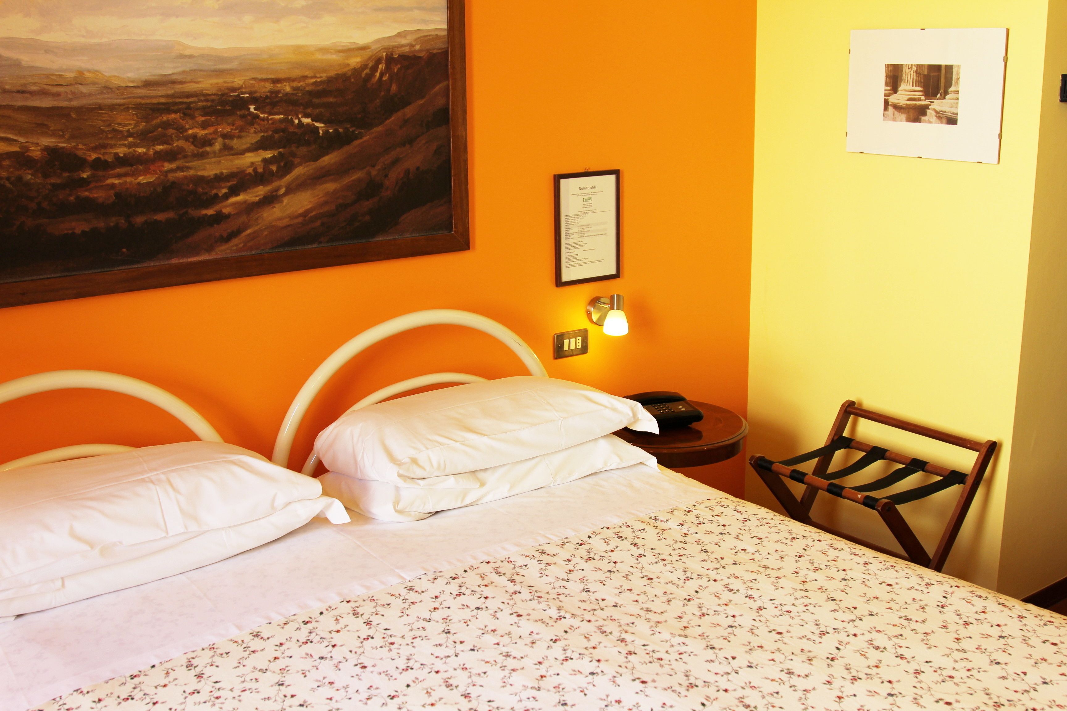 Une chambre d’hôtel avec un lit, des oreillers, une table de chevet, une lampe, une chaise et un tableau au mur.