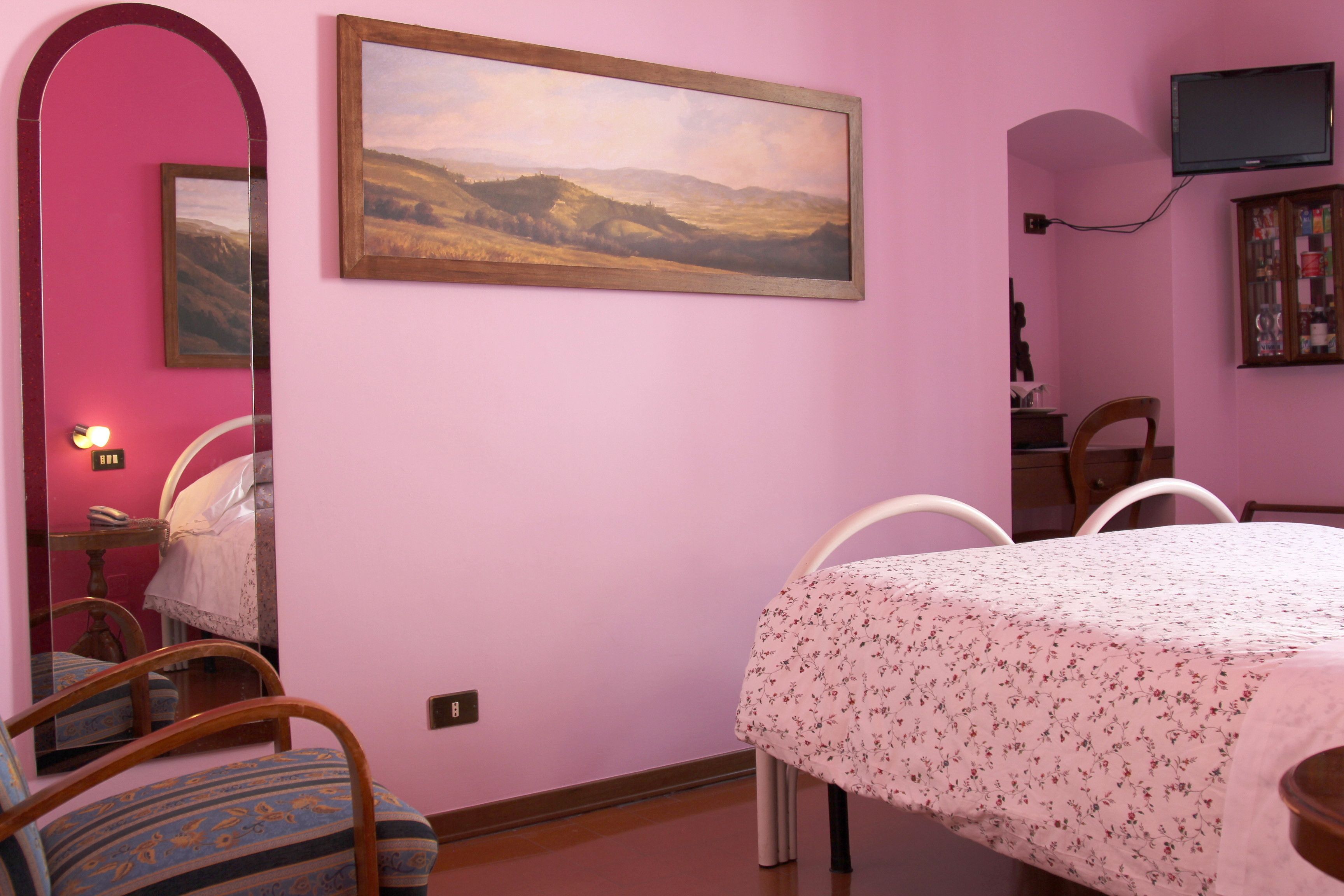 Ein Zimmer mit einem Bett, einem Sessel, einem Tisch, einem Bild und einem Fernseher an der Wand.