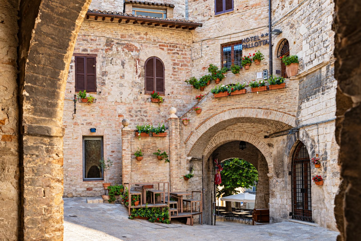 A historic stone building with a courtyard, outdoor seating, and potted plants.