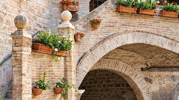 Un edificio in pietra con un cartello che riporta 'HOTEL PALLOTTA'. Molti vasi con piante adornano la facciata, e in primo piano si trova una zona con panche in legno.