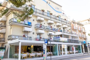 A hotel with outdoor seating, a parking sign, and multiple balconies with plants. - Hotel Jesulum (Jesolo)