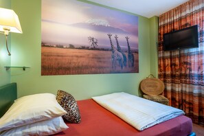 A hotel room with a bed, pillows, a wall-mounted TV, and a large painting of giraffes. - Hotel Arosa - Düsseldorf Oberkassel (Düsseldorf)