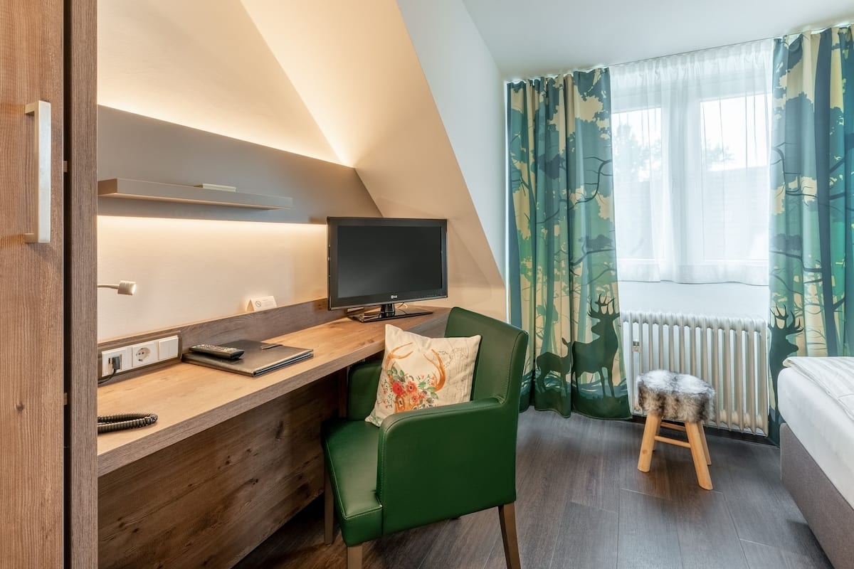 Une chambre moderne équipée d’un bureau, d’une chaise, d’une télévision et d’une fenêtre avec des rideaux.