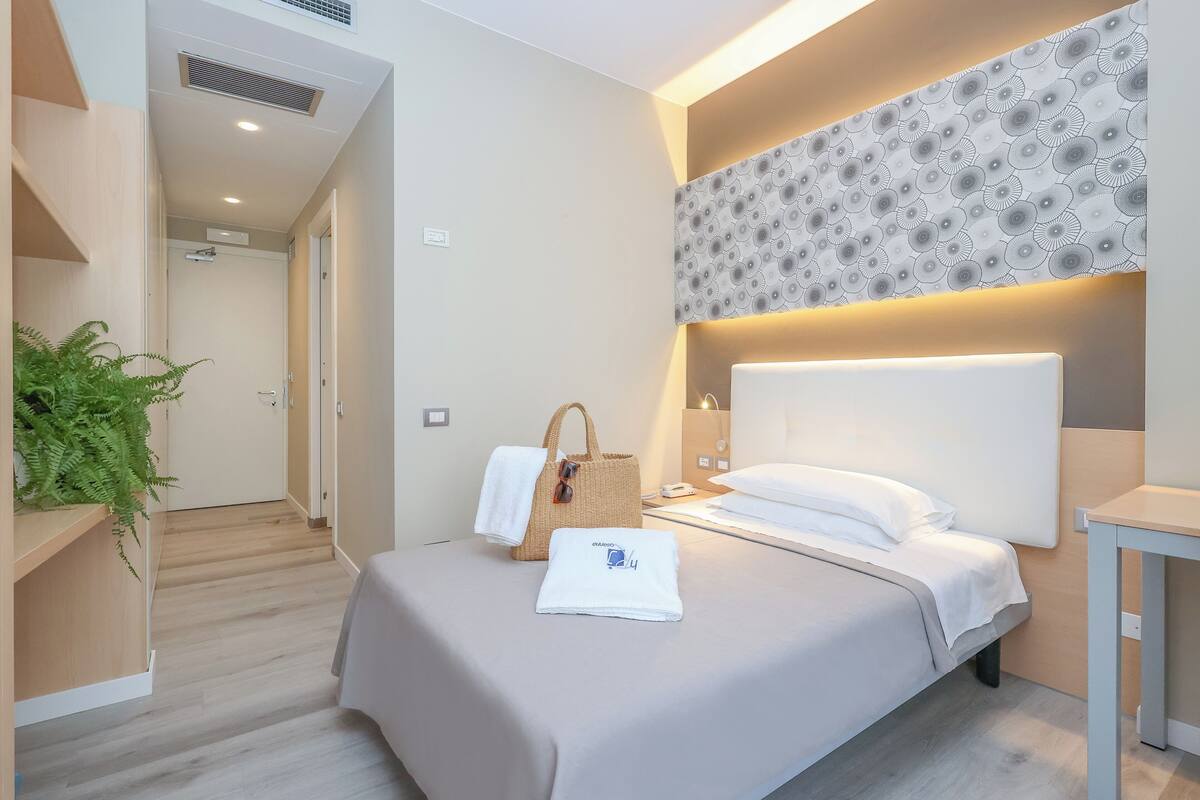Een moderne hotelkamer met een bed, nachtkastje en een wandlamp.