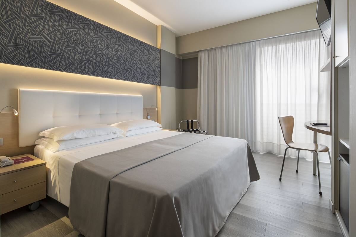 Een moderne hotelkamer met een groot bed, nachtkastjes, een stoel en een kleine tafel.