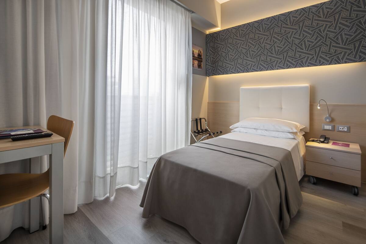 Een hotelkamer met een bed, nachtkastje en bureau met stoel.