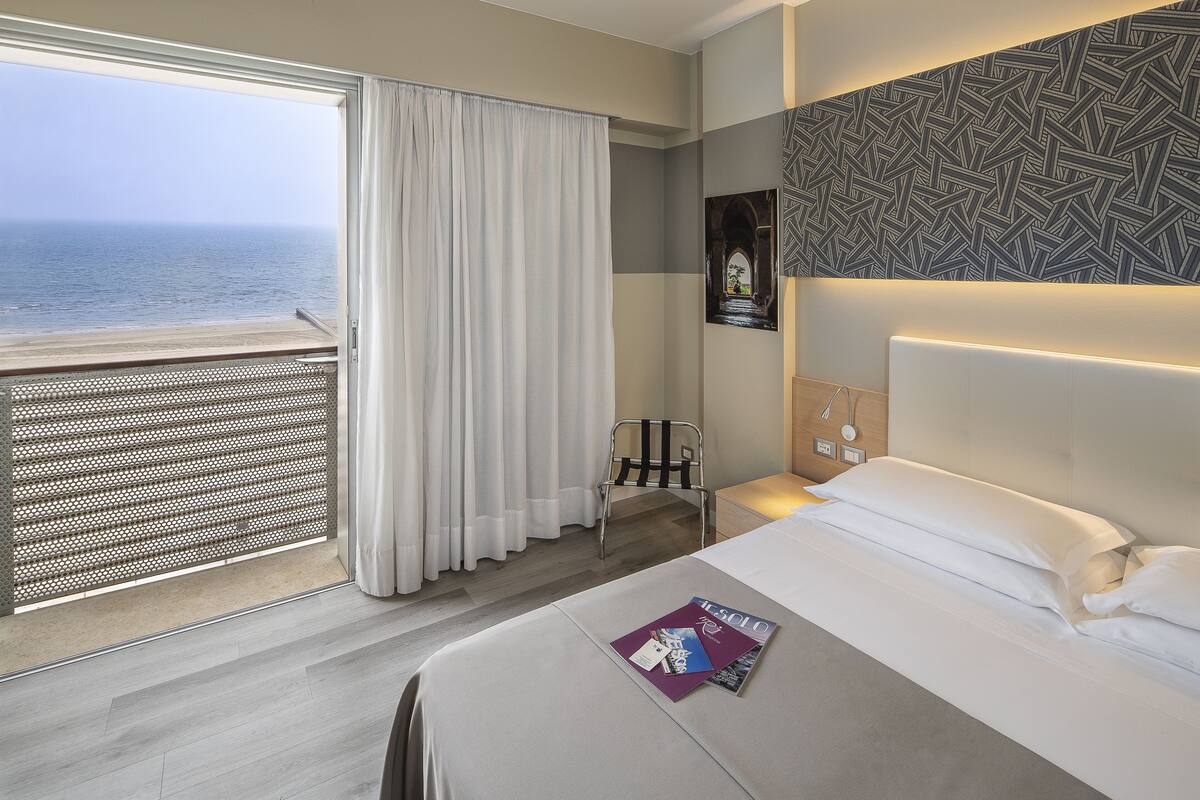 Een hotelkamer met een bed, een stoel, uitzicht op zee en een behang met patroon.