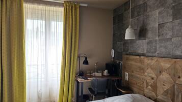 A hotel room with a bed, desk, chair, and a stone-textured wall.