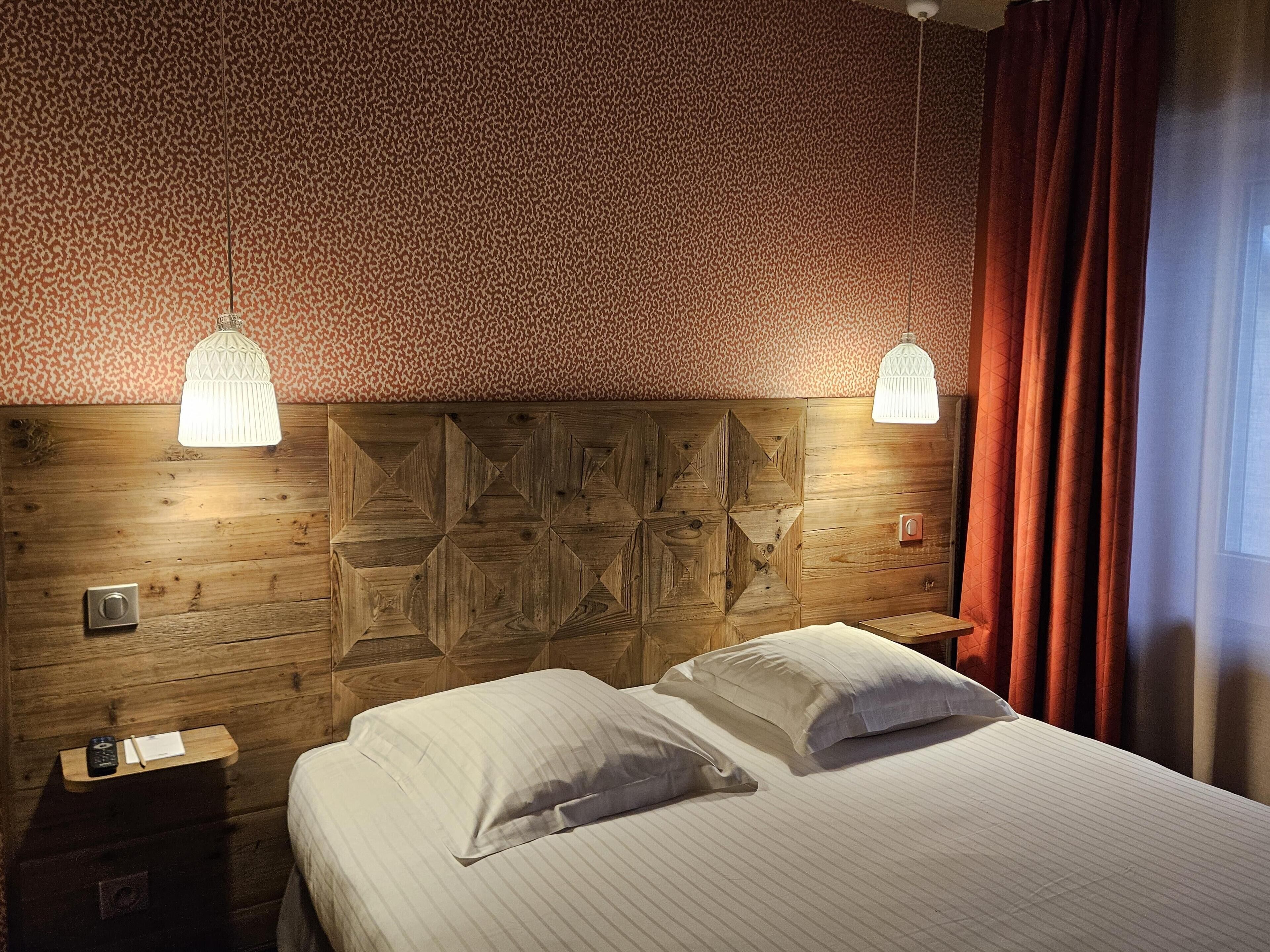 A room with a wooden headboard, two bedside lamps, a bed with pillows, a nightstand, and a window with curtains.