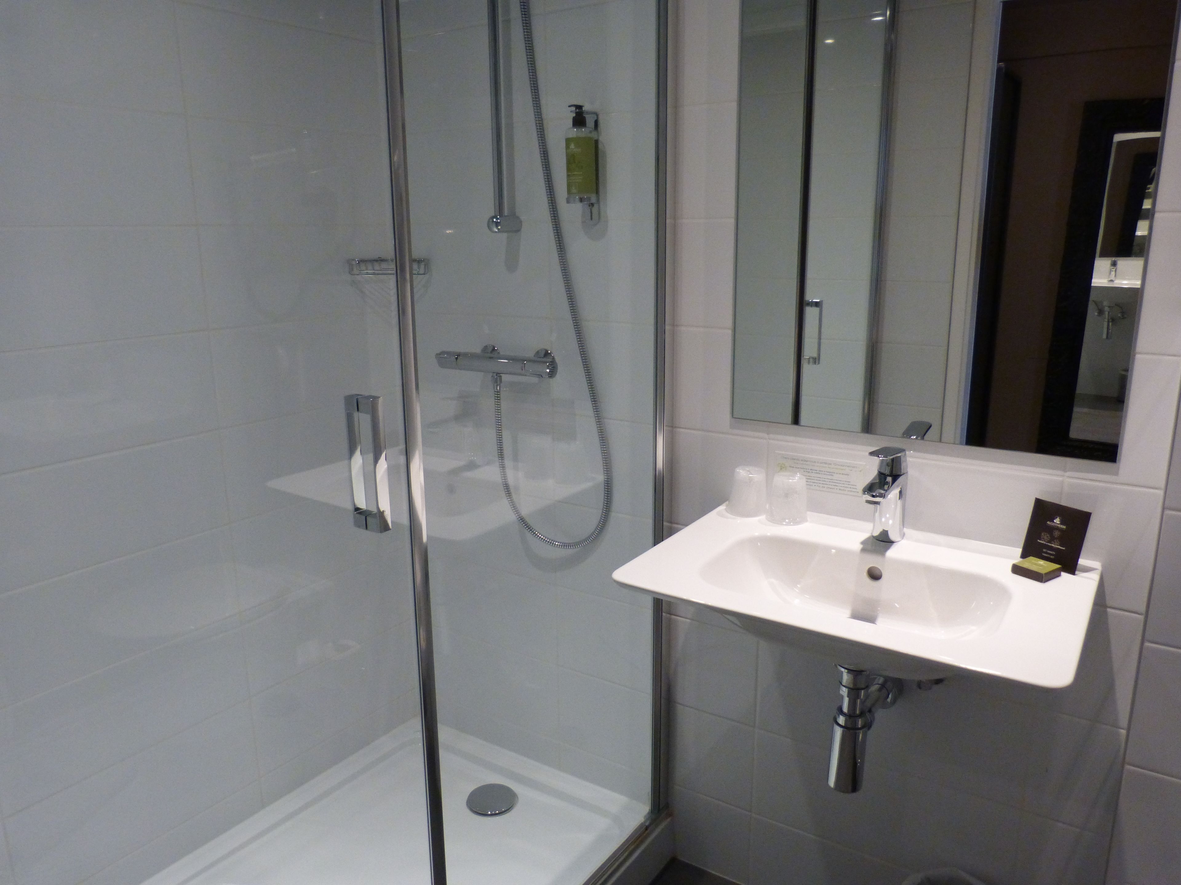 Un baño moderno con ducha de vidrio, un lavabo blanco y un espejo encima.