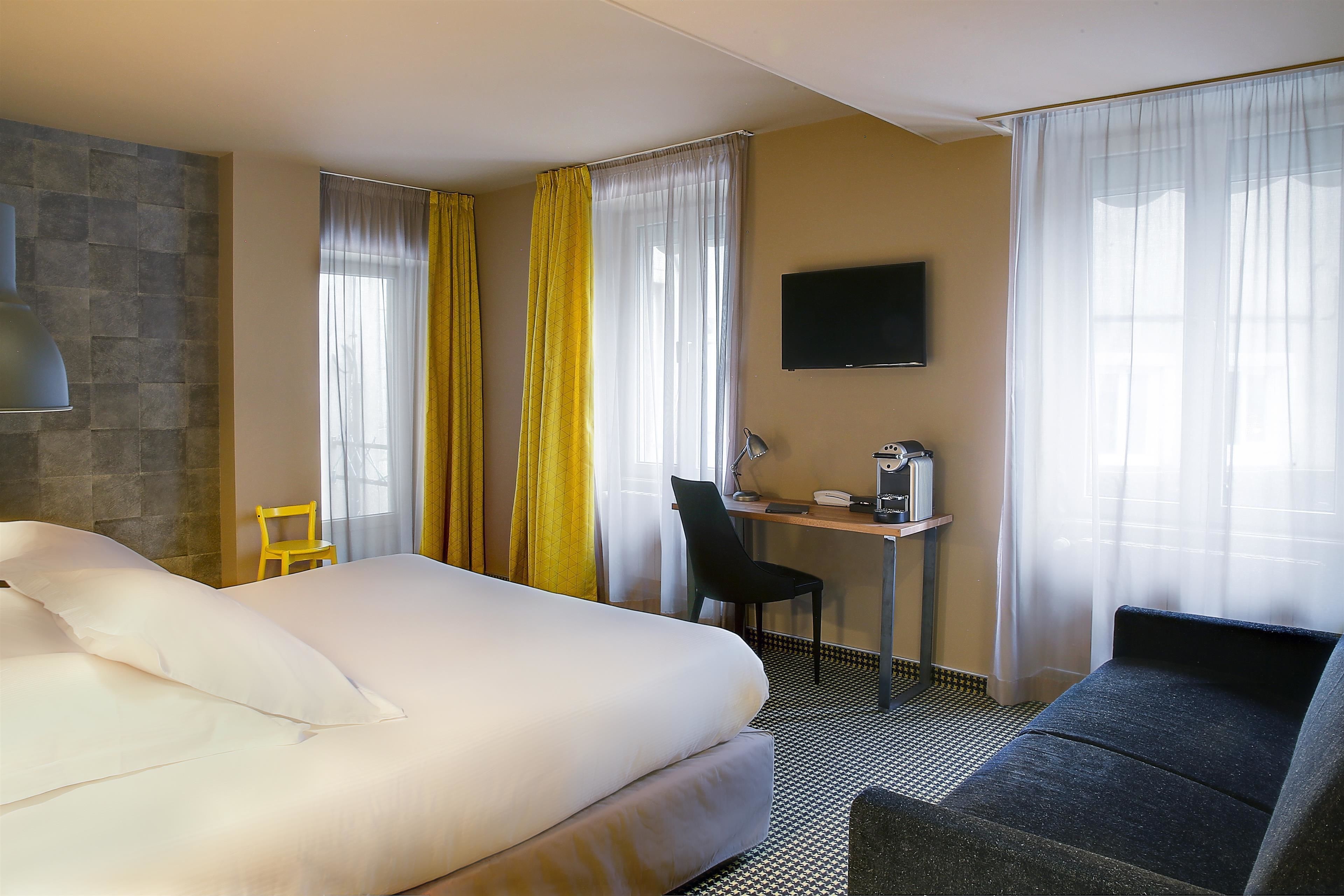 Une chambre d’hôtel avec un lit, un bureau et une chaise, une télévision et des rideaux.