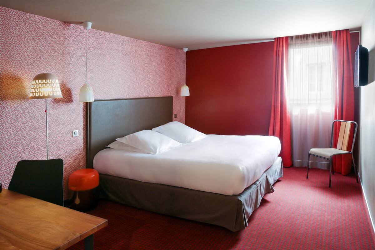 A hotel room with a bed, a desk, a chair, and a TV.