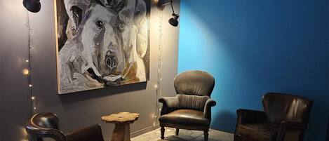 A room with a large abstract painting, leather armchairs, a small wooden table, and string lights.