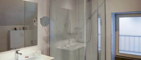 A modern bathroom with a glass-enclosed shower, a white sink, and a large mirror.
