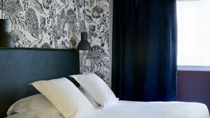 A neatly made bed with white linens and pillows, a dark headboard, and a wall with a floral pattern.