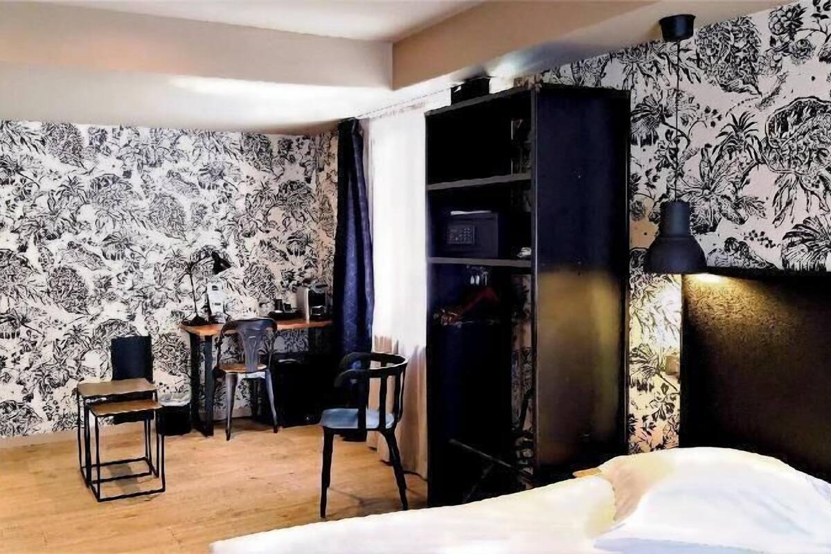 A hotel room with a bed, a desk, two chairs, a wardrobe, and a lamp.