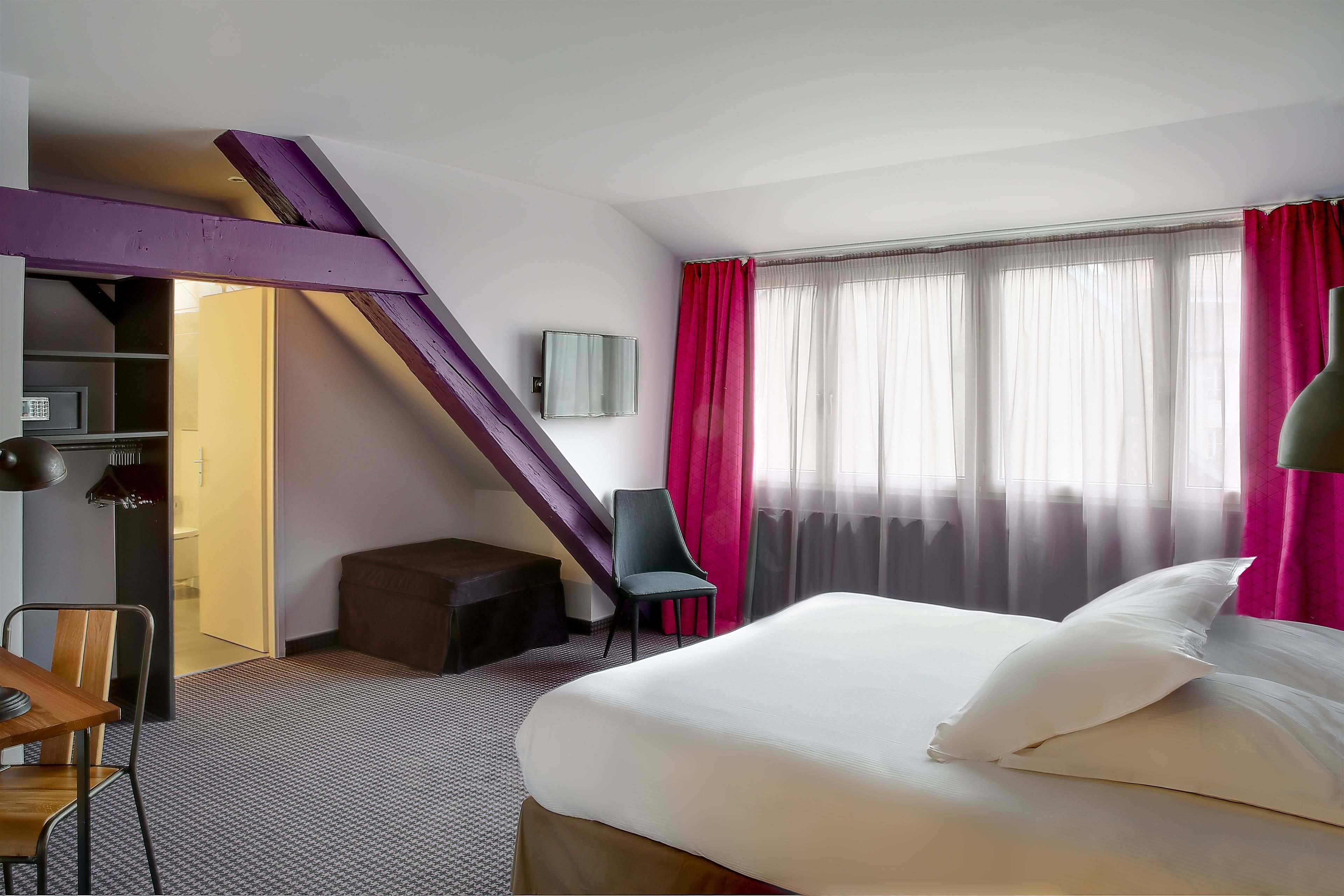A hotel room with a bed, a desk, a chair, a TV, and a staircase.