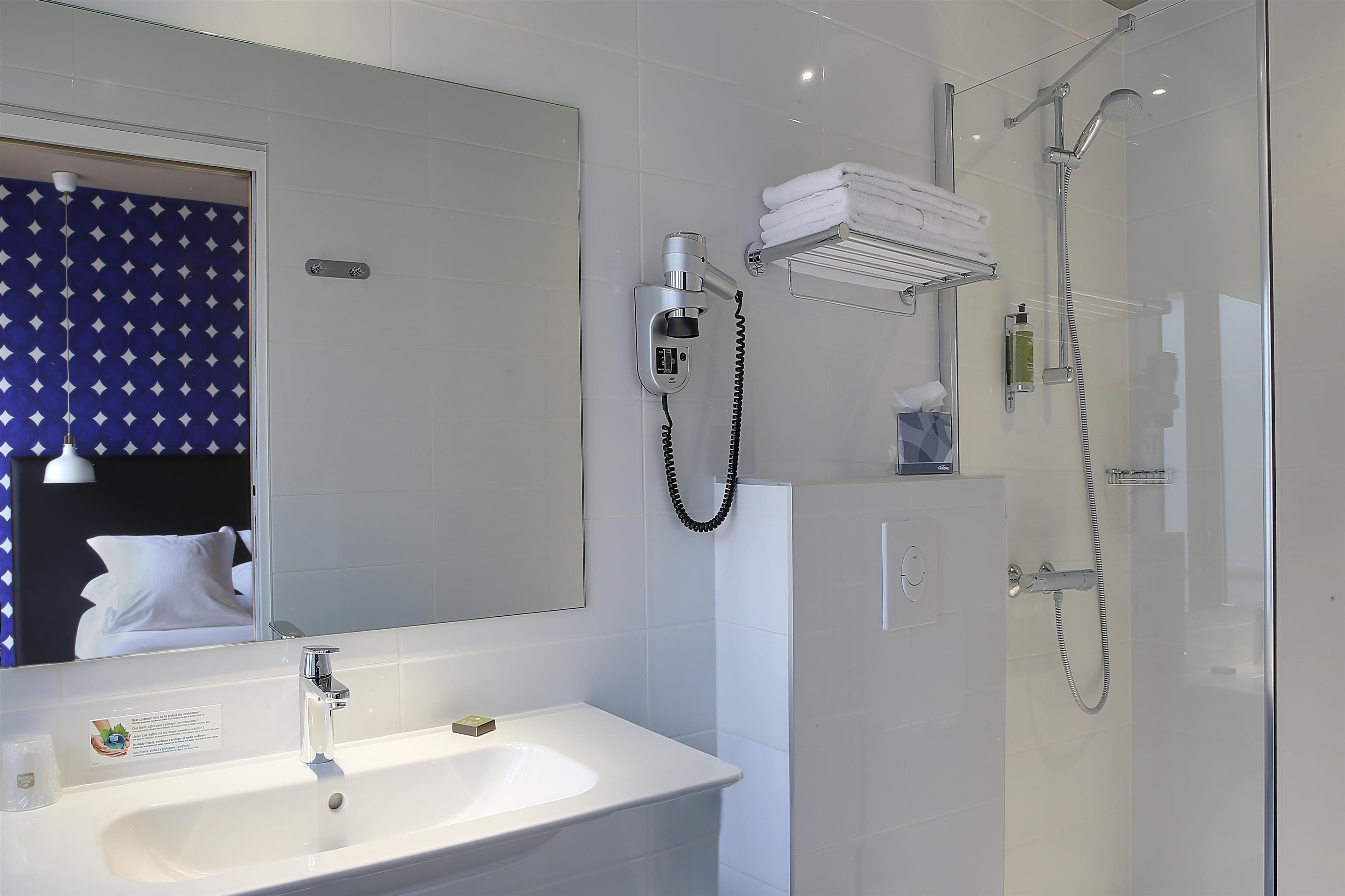 A modern bathroom with a white sink, a mirror, a shower with a glass door, and a towel rack.