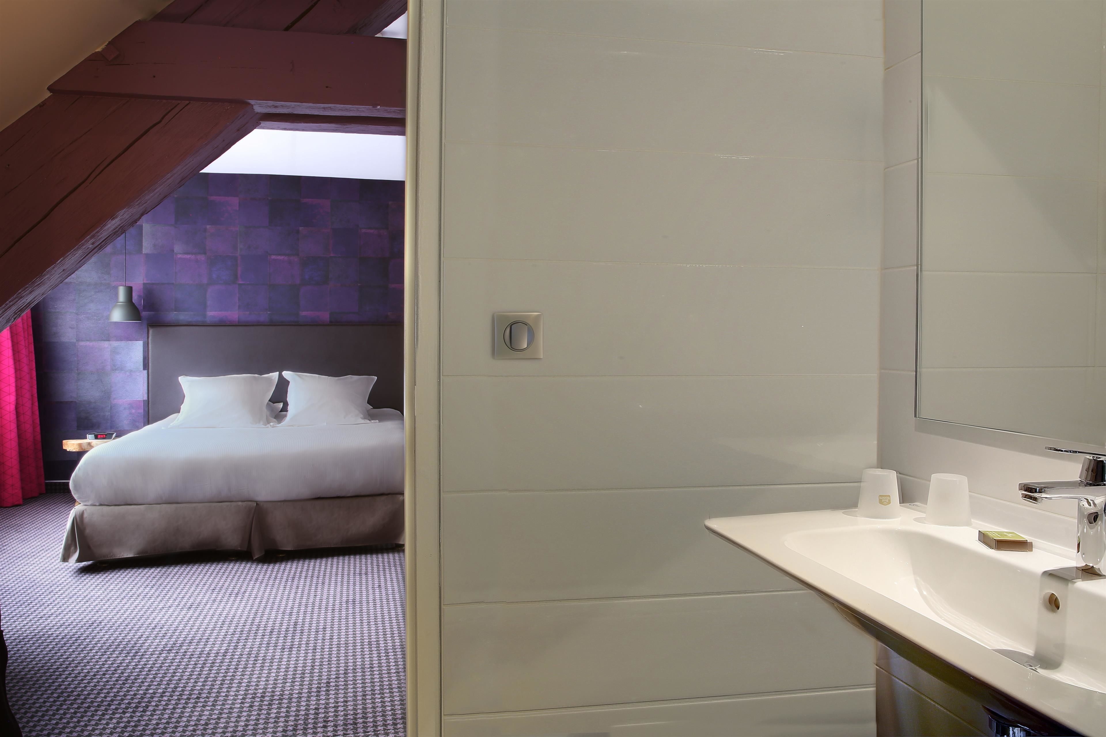 Una habitación de hotel con una cama, un baño con lavamanos y un espejo grande.