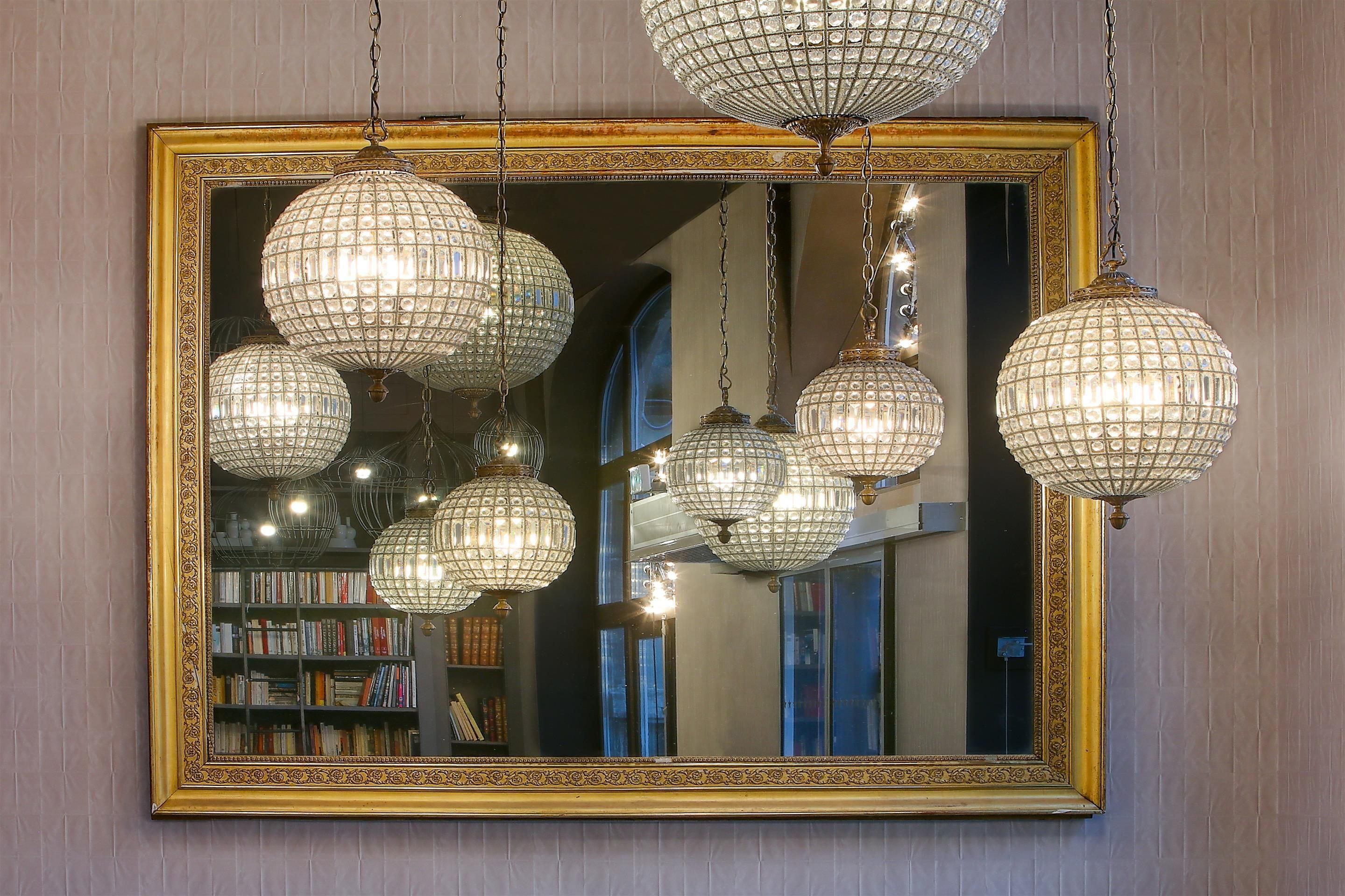 A large mirror with a gold frame reflecting multiple crystal chandeliers and a bookshelf.