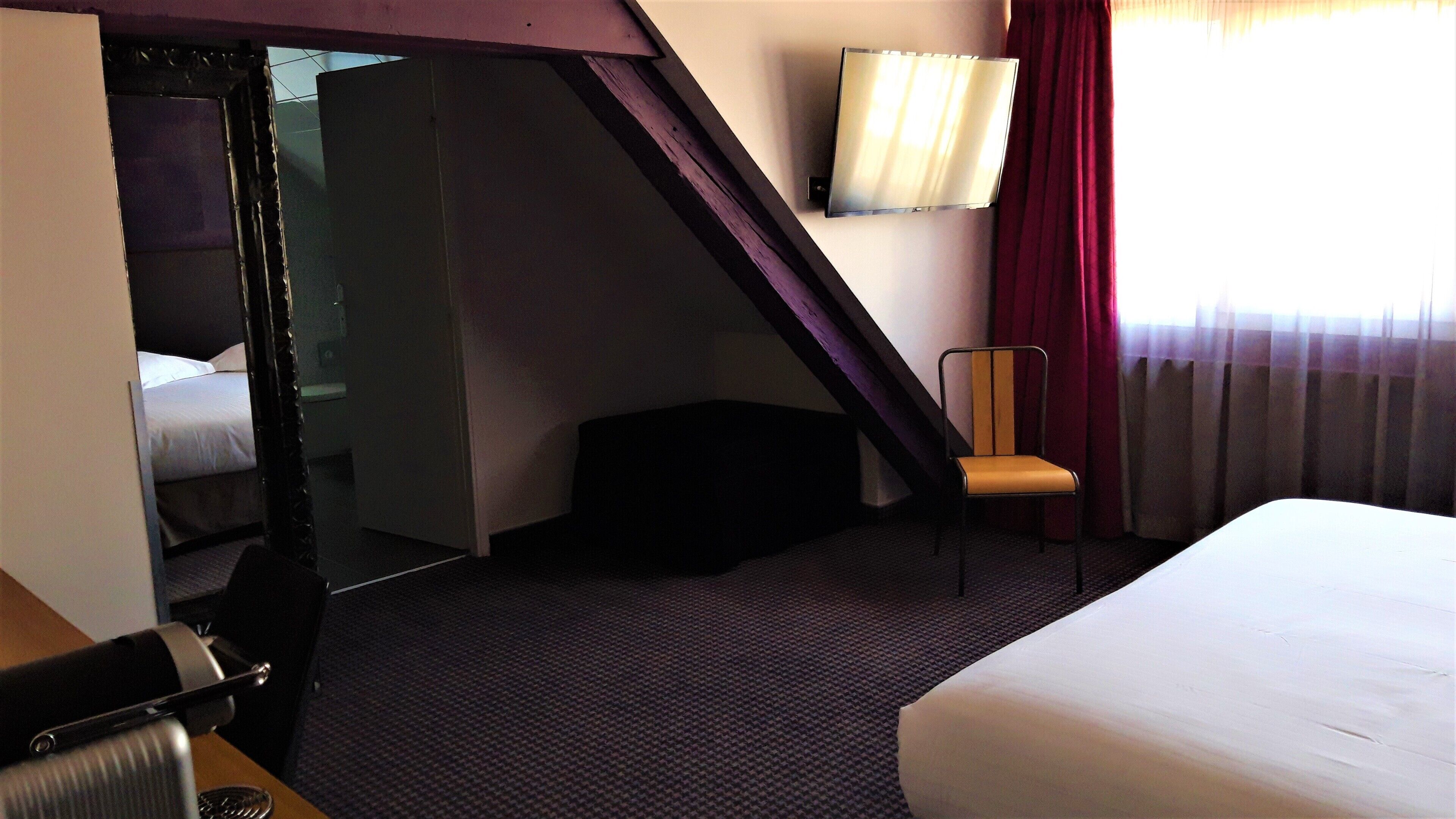 Een hotelkamer met een bed, een stoel, een bureau en een spiegel.