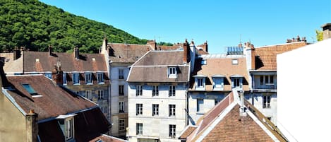 A European town with terracotta-roofed buildings, narrow streets, and a hillside in the background.