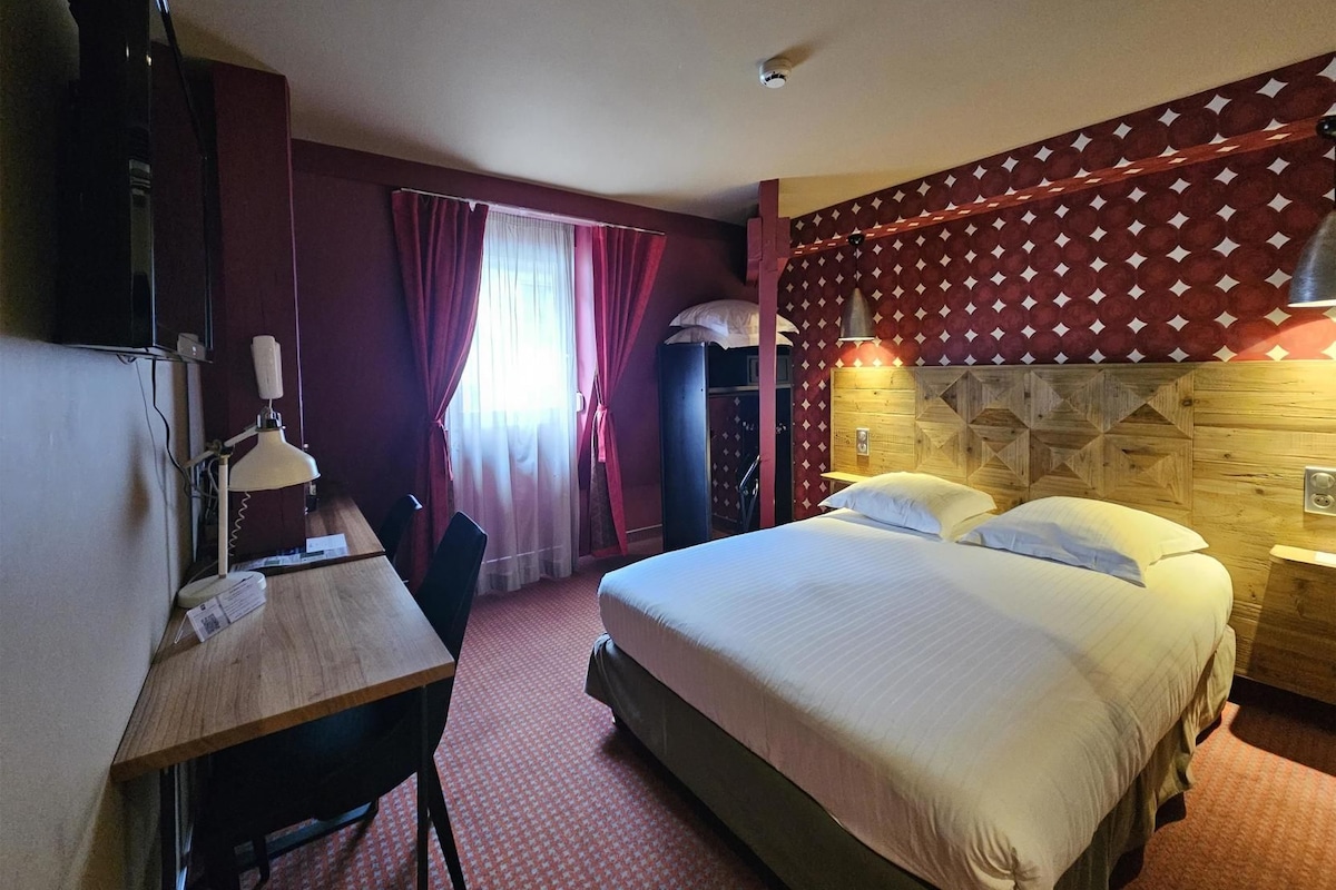 A hotel room with a bed, a desk, a chair, a television, and a window with curtains.