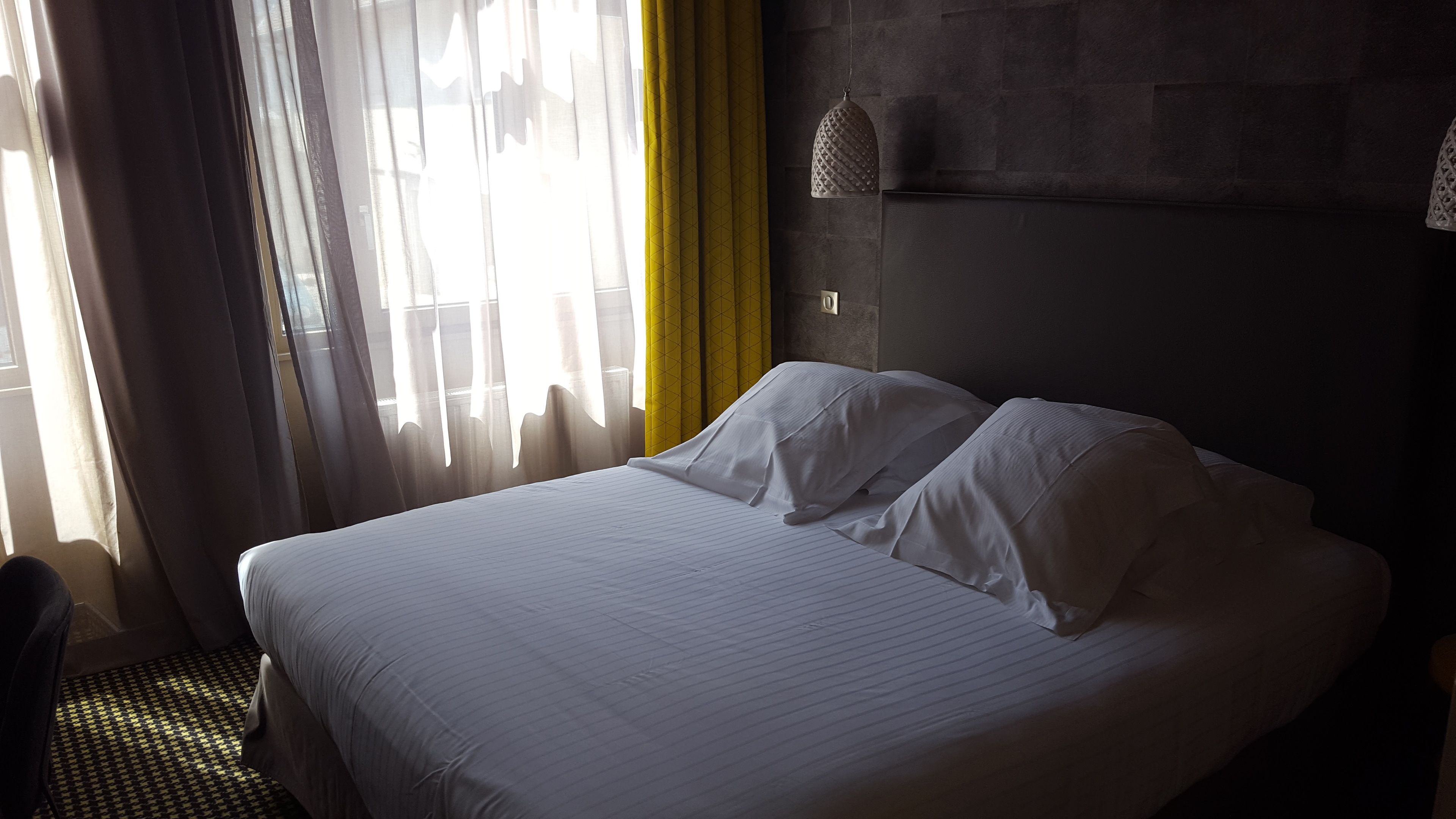 Een hotelkamer met een groot bed, een hoofdeinde en een raam met gordijnen.
